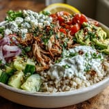 Golden rotisserie chicken and vibrant steamed broccoli florets are arranged over hearty grains, drizzled with sriracha mayo for a spicy, savory finish.