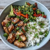 Savory chicken and rice bowl with tender marinated chicken, fluffy white rice, and crisp broccoli and bell peppers, served hot in a ceramic bowl.  