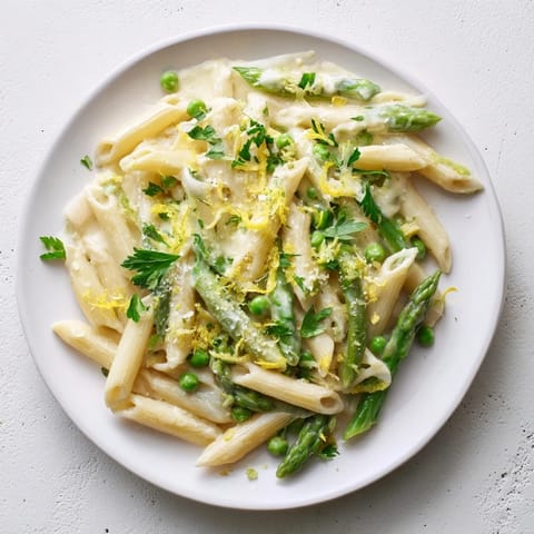 A close-up of Garlic Parmesan Spring Vegetable Pasta, featuring penne coated in a light cream sauce with tender spring vegetables.  