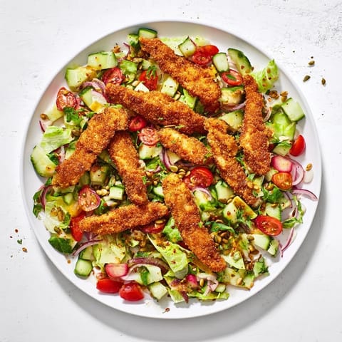 Golden chicken strips glisten with hot honey atop fresh romaine, tomatoes, cucumber, and crunchy roasted seeds in a vibrant salad.
