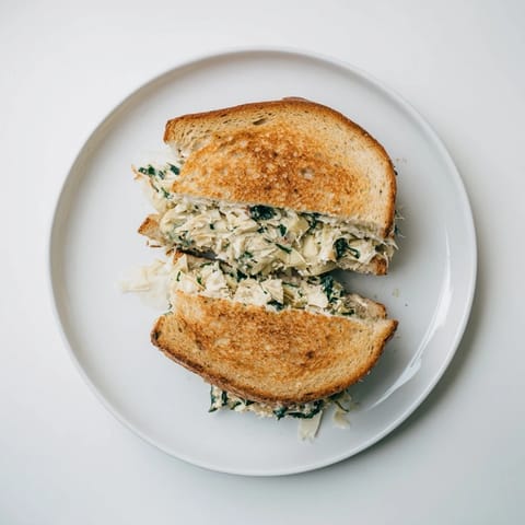 A freshly grilled artichoke spinach grilled cheese rests beside a bowl of warm tomato soup.