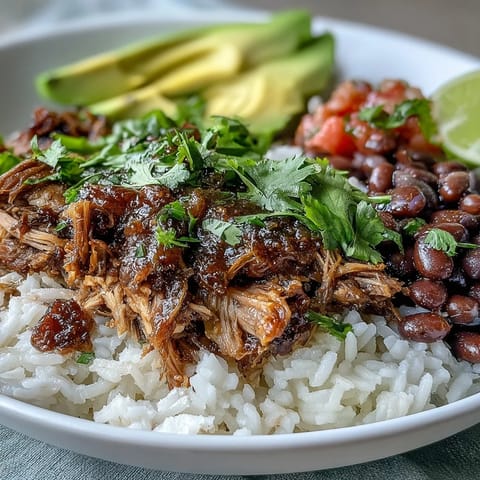 Golden-brown slow-cooked carnitas are piled high on fluffy white rice and pinto beans in this hearty Carnitas Bowl, topped with fresh salsa and creamy avocado slices.