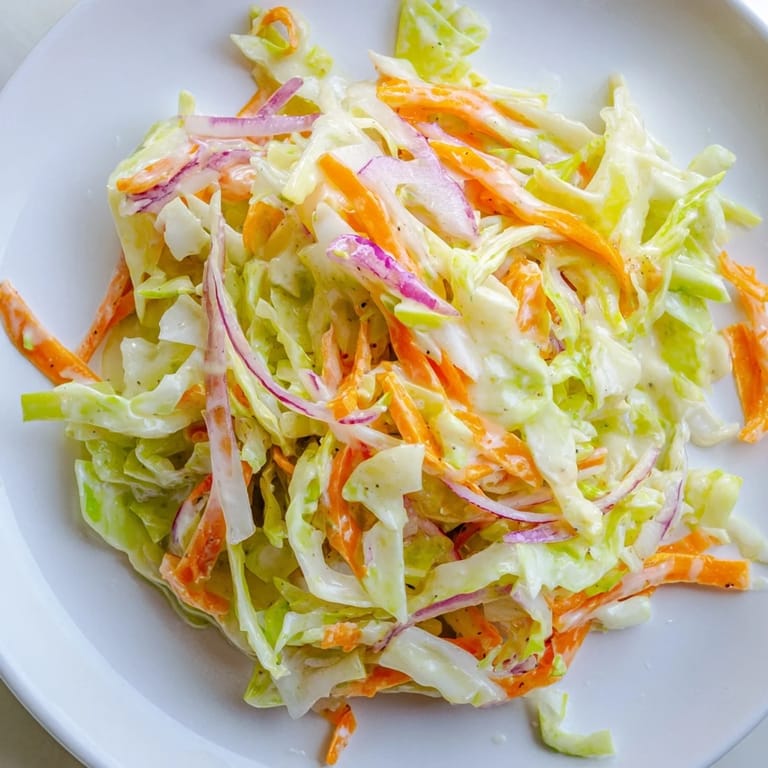Close-up of freshly made coleslaw, showing the tender shredded cabbage in a tangy, bright dressing.