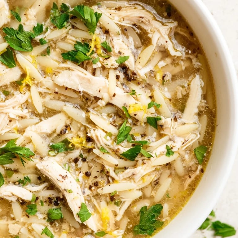 Homemade Lemon Pepper Chicken Orzo Soup with orzo pasta and vegetables in a ladle, ready to serve.