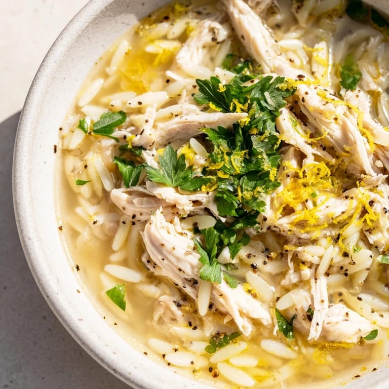 A steaming bowl of Lemon Pepper Chicken Orzo Soup garnished with fresh parsley and lemon wedges on a wooden table.