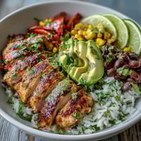 Golden Cajun-spiced chicken slices rest on fluffy white rice with colorful peppers, black beans, and sweet corn in a bowl.