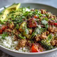Roasted vegetables and seasoned ground turkey over brown rice in a vibrant bowl, topped with creamy avocado slices and fresh cilantro.