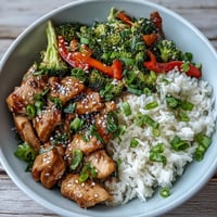 Savory chicken and rice bowl with tender marinated chicken, fluffy white rice, and crisp broccoli and bell peppers, served hot in a ceramic bowl.  